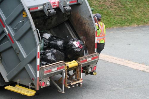 Image of waste management worker riding a garbage truck
